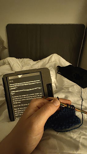 Me, lying in bed with the beginning of a crochet  piece on my lap and the pattern on my Kobo Reader in the background